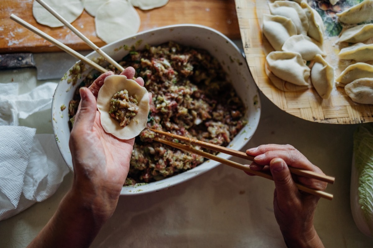 Hands folding homemade dumplings at a kitchen table